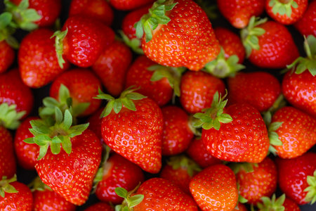 Closeup view of fresh red strawberries with green leaves arranged in a pile, highlighting their...