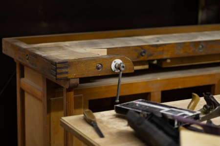 Close up of vintage wooden workbench with metal vise and carpentry tools in traditional workshop interior. Professional woodworking equipment and craftsmanship atmosphere in artisan studioの写真素材