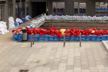 Rows of colorful sandbags placed along an urban walkway to protect modern buildings from rising river water during a city flood. Disaster prevention and temporary flood defense