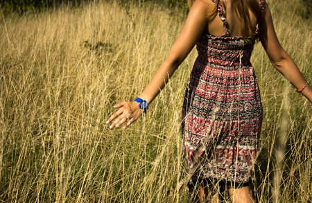 Young beautiful girl walking in the field and runs a hand through the high dry grass at summertimeの写真素材