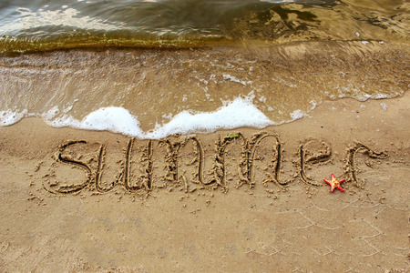 Inscription summer with red starfish on the sand by the sea with waves.の写真素材