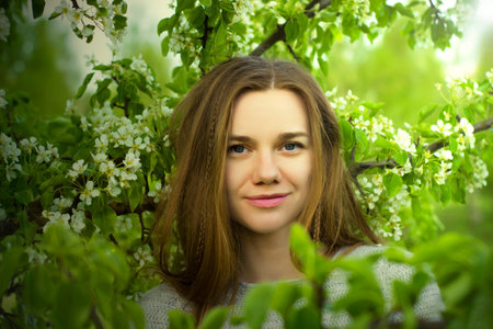 Portrait of beautiful young girl close up among a blossoming tree with green leaves outdoors.の写真素材