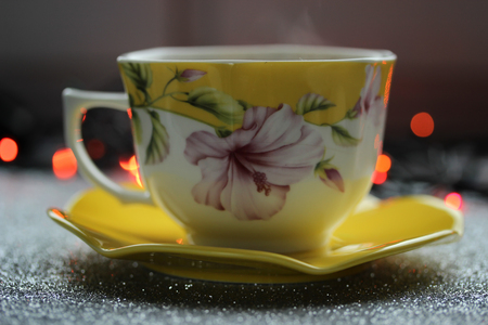 Beautiful aromatic and hot cup of coffee with saucer near the window early at the morning on the colored lights backgroundの写真素材