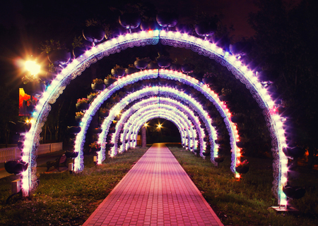 Bright glowing arch of colored lanterns in the park in the eveningの写真素材