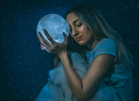 Young pretty woman with the full moon and clouds on the starry blue background closeup.Art processingの写真素材