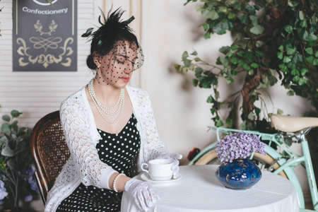 Young pretty woman dressed up into retro style is sitting in the street cafe with cup of coffee and croissant.の写真素材