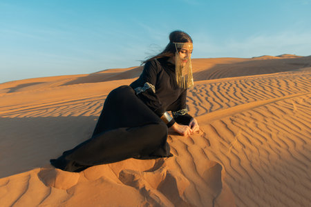 Beautiful woman in brilliant Burqa mask among the Dubai desert at sunset timeArabian style.の写真素材