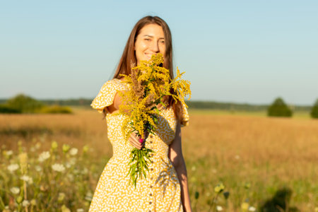 Young beautiful woman in yellow dress closeup with yellow field flowers in hand on the natural background in summertime.の写真素材