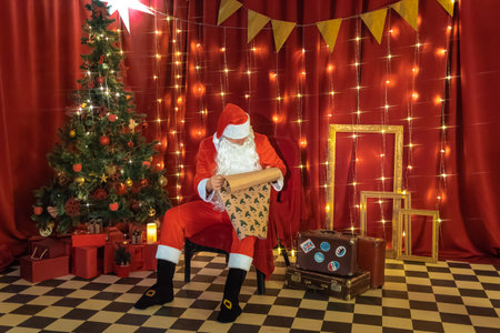 Santa Claus sitting on a chair in a room decorated for Christmas.の写真素材