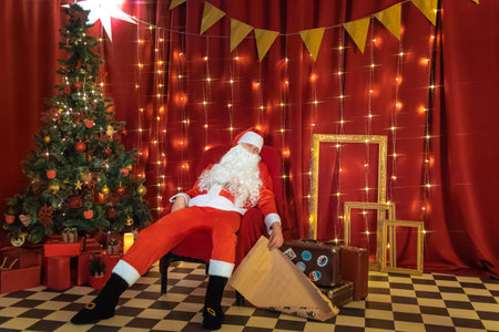 Santa Claus sitting on a suitcase in a room with a Christmas treeの写真素材