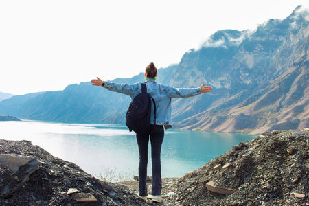 Young woman with backpack standing on top of mountain and looking at lakeの写真素材