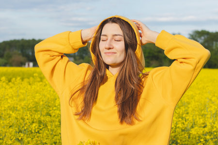 Portrait of a young woman in a yellow hoodie on the background of a blooming rapeseed field