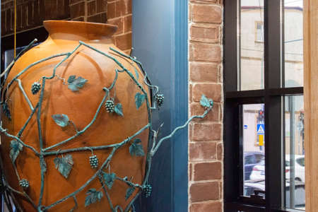 A large ceramic wine jug decorated with copper vines is used in the interior of the cafe. At the window of the cafe there is a traditional Georgian terracotta jug for storing grape wine.の写真素材