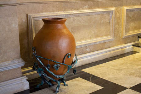 A large ceramic wine jug with copper vine decor sits on the floor of a cafe. A traditional Georgian jug is used in the interior of the cafe.の写真素材