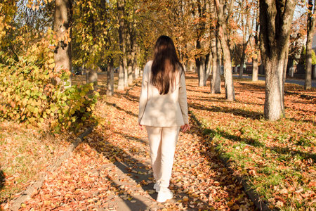 Rear view of elegant young woman with long dark hair in casual tracksuit in autumn. Cute model walks in the park in golden autumn on the background of nature. Autumn Walk.の写真素材