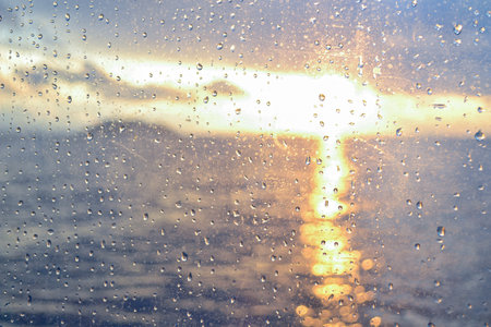 View of a sea sunset through raindrops on a window pane. Raindrops on window pane on sea sunset background.の写真素材
