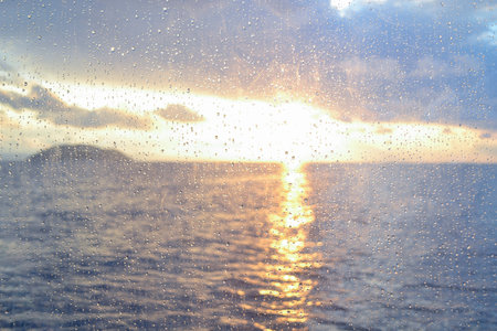 View of a sea sunset through raindrops on a window pane. Raindrops on window pane on sea sunset background.の写真素材