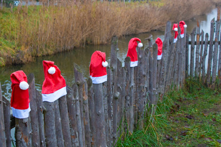 Santa Claus hats on a wooden fence in a rural setting. Outdoor Christmas decorationsの写真素材