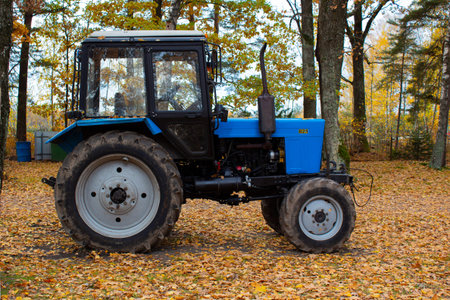 A blue tractor parked in a clearing with fallen leaves against a background of trees. Autumn landscape in the village.の写真素材
