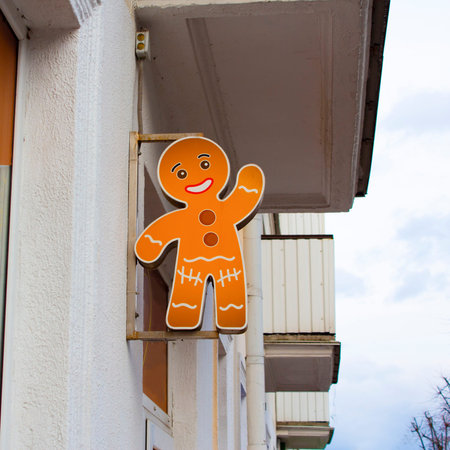 A sculpture of a gingerbread man hangs on the wall of a house on the street. Street decor for a...