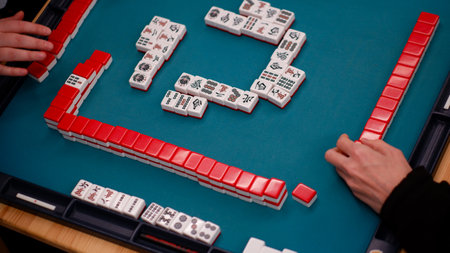 A mahjong table with an active game and the hands of a participant in the game. An ancient Asian game called Mahjong as a way to relax and have fun. Fragment of the game.の写真素材