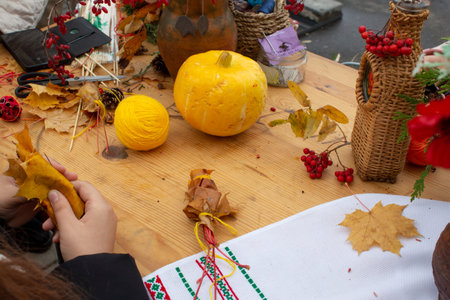 Making Halloween decorations. A girl is making a rose from maple leaves. Small pumpkins are on the...