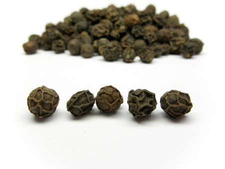 Corns of black pepper with heap of black pepper on background