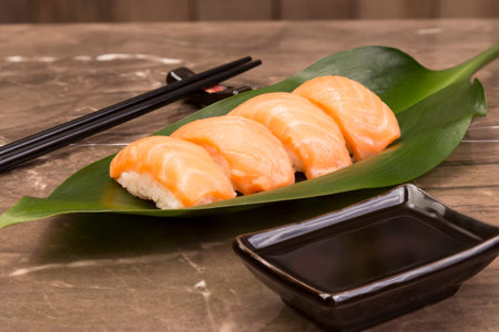 Sushi syake set on green leaf with soy sauce and sticks on brown marble stone tableの写真素材