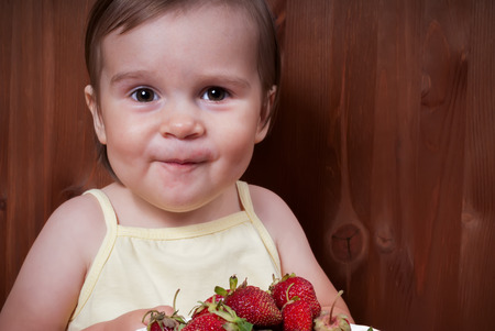 Portrait of the happy little girl eating strawberries at homeの写真素材