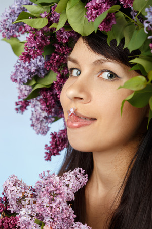 Beautiful young model woman with lilac bouquet and wreath as flowers hair style on blue backgroundの写真素材