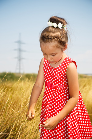 Cute little girl in the red dress in a fieldの写真素材