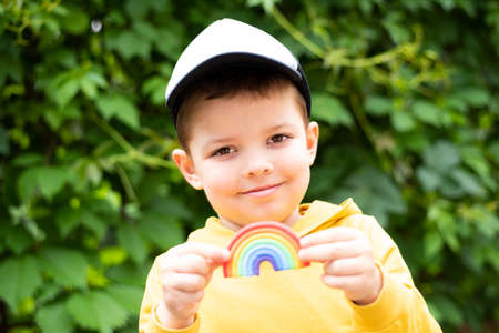 A cute baby boy smiles and holds a plasticine rainbow in his hands on a background of green leaves.の写真素材