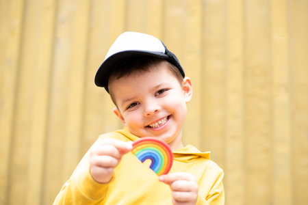 A cute baby boy smiles and holds a plasticine rainbow in his hands on a yellow background.