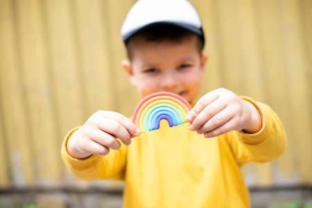 A cute baby boy smiles and holds a plasticine rainbow in his hands on a yellow background.の写真素材