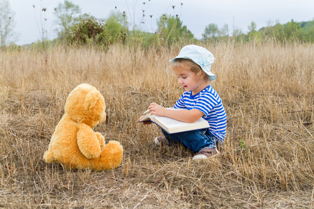Cute girl reading book Teddy bear on the grass.の写真素材