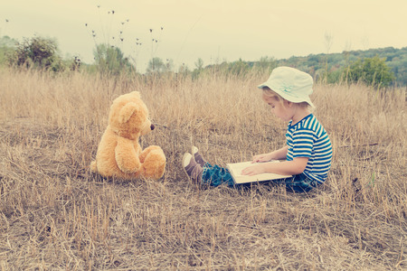 Cute girl reading book Teddy bear on the grass.の写真素材