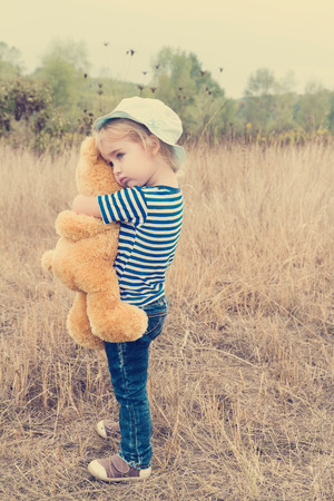 Cute little girl standing in the grass hugging a Teddy bearの写真素材