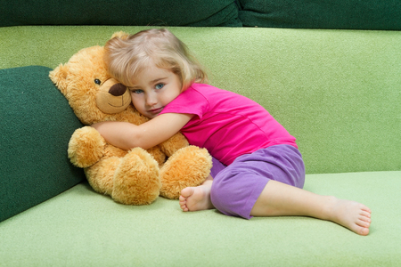 Little girl hugging Teddy bear on a green soft couch.の写真素材