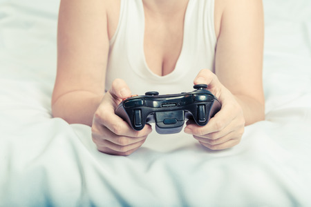 Young caucasian woman playing video game console lying on the bedの写真素材