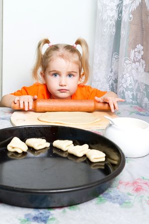 Little girl making dough in the kitchen with a rolling pin.の写真素材