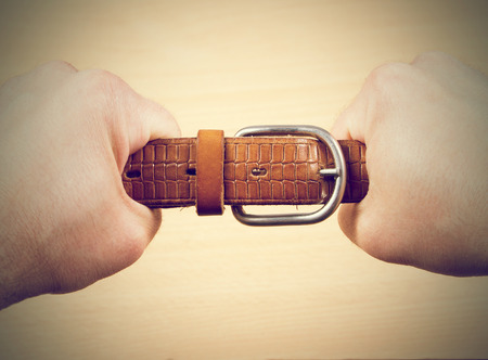Two hands pulling a leather belt in opposite directions isolated on wood backgroundの写真素材