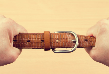 Two hands pulling a leather belt in opposite directions isolated on wood backgroundの写真素材