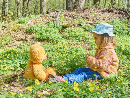 Cute girl playing with an Teddy bear on the grass in forest. Flower meadowのeditorial素材