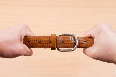 Two hands pulling a leather belt in opposite directions isolated on wood background
