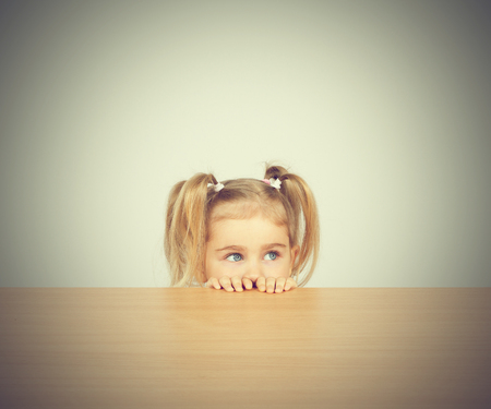 Little girl in casual clothes looking up and thinking. Sitting at the table.の写真素材