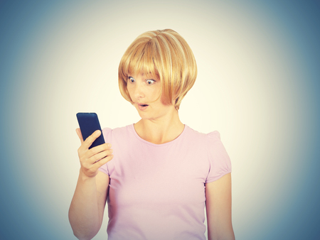 Closeup portrait anxious  young woman looking at phone seeing bad news. Blonde girl in horror reading sms on your smartphone isolated on  background.の写真素材