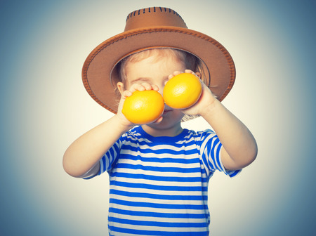 Little Funny girl in striped shirt and hat keeps lemons. Isolated on white backgroundの写真素材