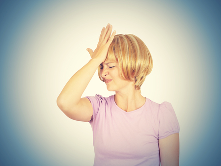 Witless young woman holding her hand to her forehead. Blonde girl forgot. Stupid fool. Isolated on background.の写真素材