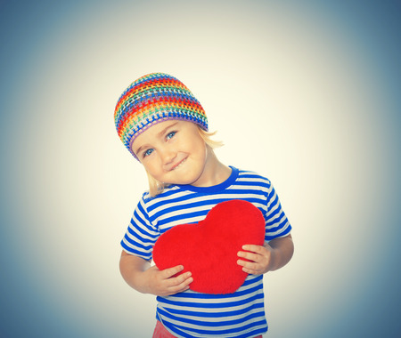 Little girl holding a red heart toy. Isolated on a white background.の写真素材
