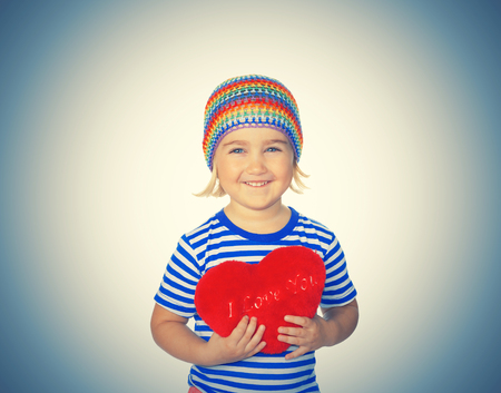 Little girl holding a red heart toy. Isolated on a white background.の写真素材